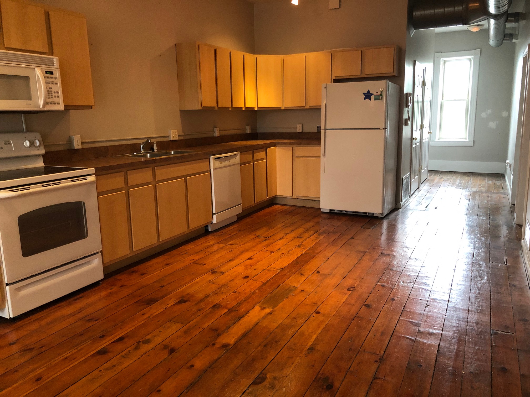 an empty kitchen with wooden floors and a refrigerator